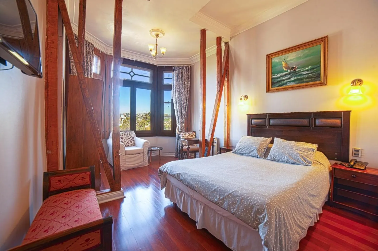 La misma habitación del bow window: vigas de madera, una banca roja, sillón y el cuadro de un velero sobre la cama.