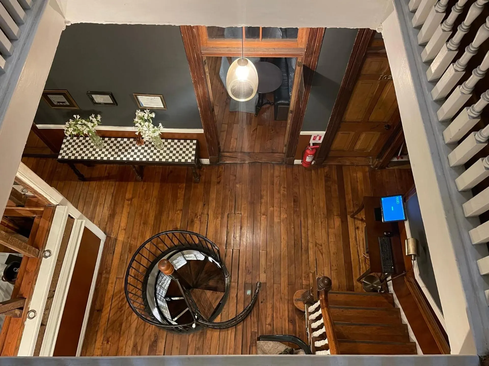 El hall visto desde el piso de arriba: piso de tablas, una escalera de caracol de fierro y una mesa con flores.