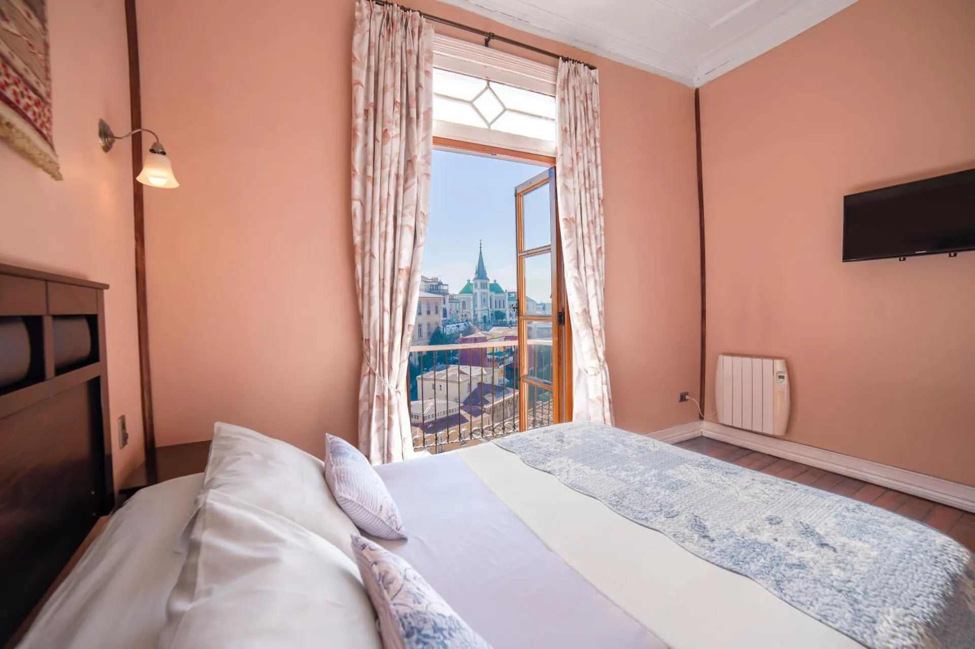 Habitación de muros rosados con una ventana alta abierta a la iglesia del cerro y la bahía.