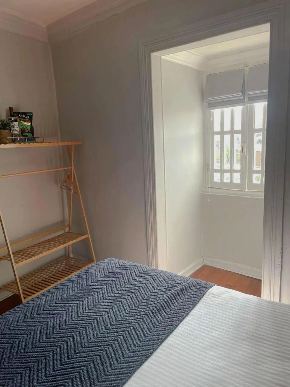 Un perchero de madera y la ventana de la Single, al pie de la cama.