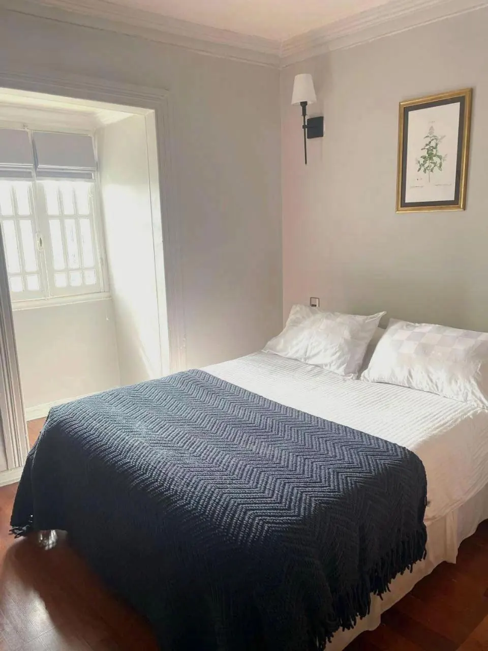 La Single: cama con cubrecama azul tejido junto a una ventana con cortina romana.